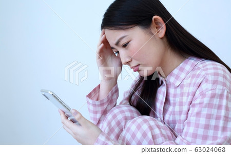 Image of a woman operating a smartphone in pajamas Image of a woman operating a smartphone in pajamas 63024068