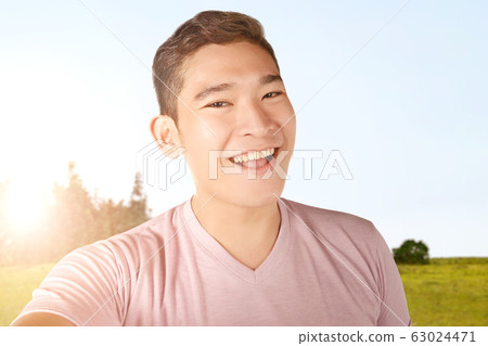 Asian man making selfie using the camera phone on the green field Asian man making selfie using the camera phone on the green field 63024471