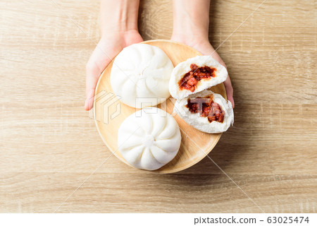 Steamed buns stuffed with red minced pork on wooden plate holding by hand 63025474