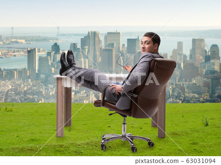 Businessman sitting on grass with city view Businessman sitting on grass with city view 63031094