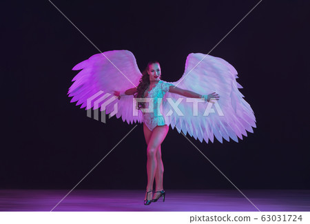 Young female dancer with angel's wings in neon light on black background 63031724