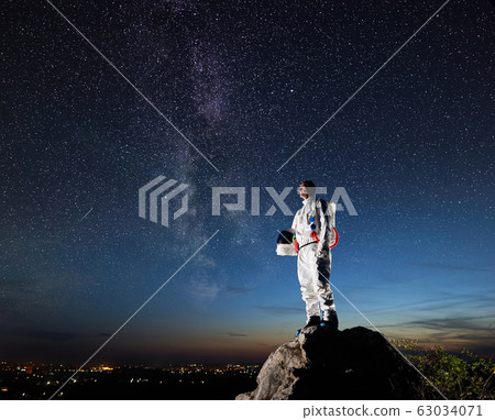 Astronaut standing on rocky mountain under night starry sky. Astronaut standing on rocky mountain under night starry sky. 63034071