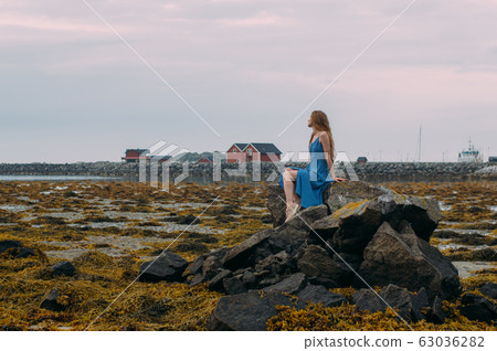 Young woman in blue dress sitting on stone among 63036282