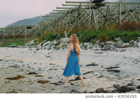 Young woman in blue dress walking on white sand, 63036283