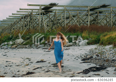 Young woman in blue dress walking on white sand, 63036285