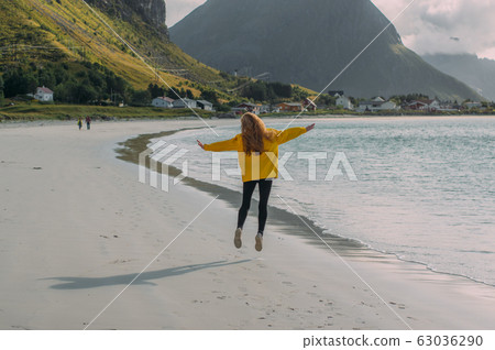 Jumping girl in yellow jacket on the white sand  63036290