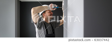 Young smiling repairman standing in empty flat and fixing electricity with screwdriver Young smiling repairman standing in empty flat and fixing electricity with screwdriver 63037442