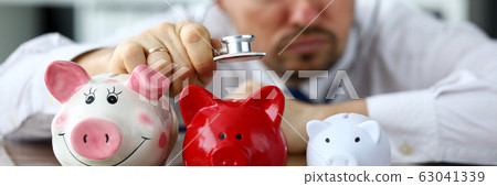 Funny businessman listen three piggybanks for cash Funny businessman listen three piggybanks for cash 63041339