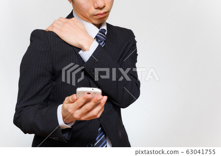 A man who operates a smartphone while holding his shoulder stiff shoulder fatigue 63041755