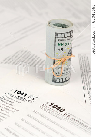 Tax forms lies near roll of hundred dollar bills. Tax forms lies near roll of hundred dollar bills. 63042569