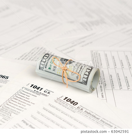 Tax forms lies near roll of hundred dollar bills. 63042591
