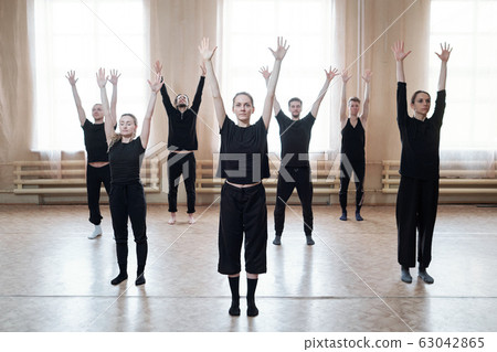 Group of young dancers in black activewear raising arms while training 63042865