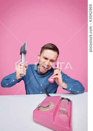 Furious young man with axe expressing rage while shouting in telephone receiver Furious young man with axe expressing rage while shouting in telephone receiver 63042969