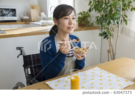Young housewife sitting on wheelchair and eating breakfast 63047373