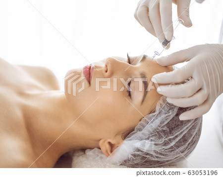 Beautician doing beauty procedure with syringe to face of young brunette woman. Cosmetic medicine and surgery, beauty injections 63053196