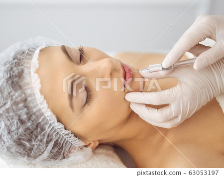 Beautician doing beauty procedure with syringe to face of young brunette woman. Cosmetic medicine and surgery, beauty injections 63053197