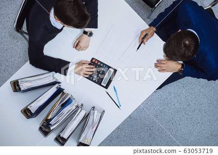 Business people at meeting, view from above. Bookkeeper or financial inspector making report, calculating or checking balance Business people at meeting, view from above. Bookkeeper or financial inspector making report, calculating or checking balance 63053719