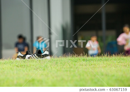 Selective focus on the grass field with blurred sneaker shoes and children running on the lawn ground in background 63067159