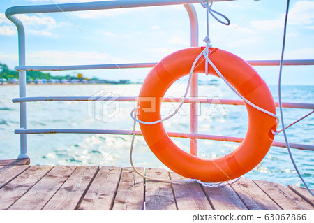 Orange lifebuoy with rope on a wooden pier near sea. 63067866