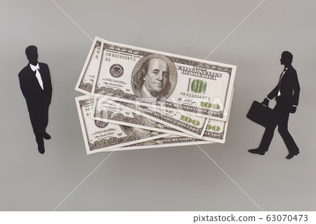 Dollars and two paper figures of businessmen. Dollars and two paper figures of businessmen. 63070473
