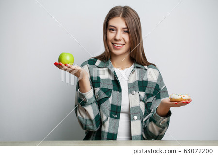 Woman makes a choice between healthy and harmful food Woman makes a choice between healthy and harmful food 63072200