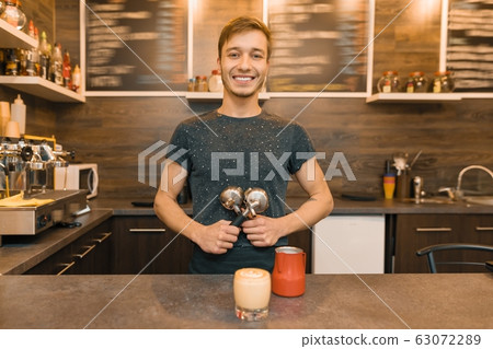 Portrait of young smiling male cafe worker, standing at the counter. Man with freshly made coffee Portrait of young smiling male cafe worker, standing at the counter. Man with freshly made coffee 63072289