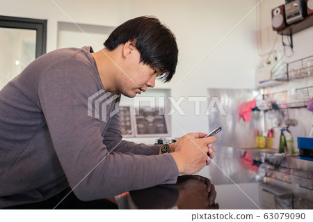 Attractive Asian man using a smartphone at the Attractive Asian man using a smartphone at the 63079090