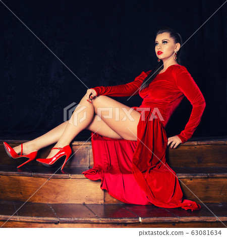 Fashion model in a sexy red dress sitting on steps Fashion model in a sexy red dress sitting on steps 63081634