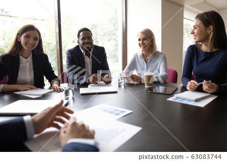 Smiling diverse colleagues laugh discussing ideas at meeting Smiling diverse colleagues laugh discussing ideas at meeting 63083744