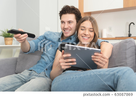 Young couple watching TV on sofa Young couple watching TV on sofa 63087869