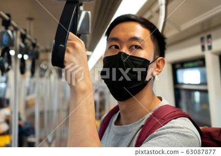 Close up of one young Asian man wearing a black surgical face mask in subway train during new type Coronavirus Covid-19 pneumonia outbreak and pm 2.5 smog air pollution crisis in big city Close up of one young Asian man wearing a black surgical face mask in subway train during new type Coronavirus Covid-19 pneumonia outbreak and pm 2.5 smog air pollution crisis in big city 63087877
