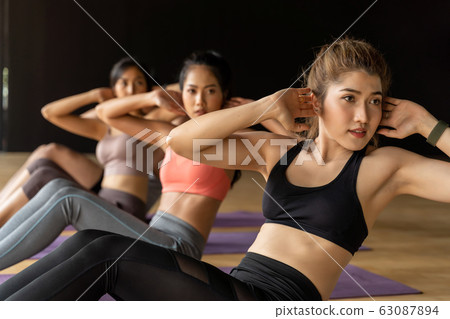 Group of Asian women and man doing abdominal exercises on yoga mats in aerobics class. Young sporty people twisting body on the floor in gym studio. 63087894