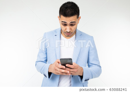 businessman in a blue jacket looks suspiciously at a smartphone on a white background businessman in a blue jacket looks suspiciously at a smartphone on a white background 63088241
