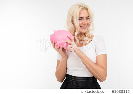 portrait of a caucasian girl in a skirt and t-shirt holding a pink piggy bank for saving money on a 63088315