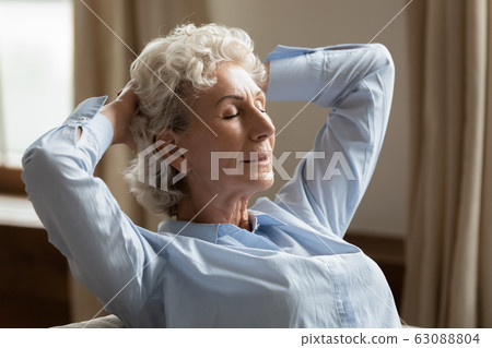 Calm senior woman relax on couch at home daydreaming Calm senior woman relax on couch at home daydreaming 63088804