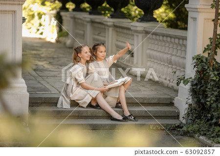 Two girls of primary school schoolgirls read a book in the courtyard of the academy Two girls of primary school schoolgirls read a book in the courtyard of the academy 63092857