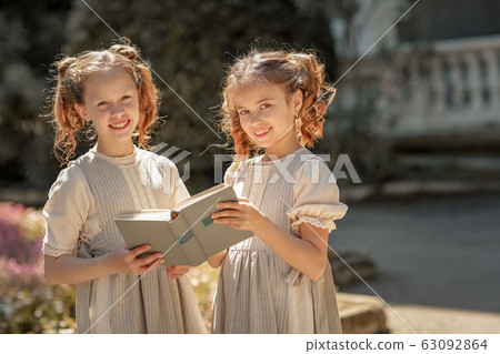 Two girls of primary school schoolgirls read a book in the courtyard of the academy 63092864