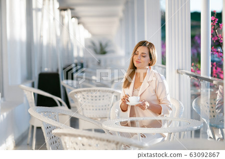 A woman sits at a table and drinks coffee 63092867