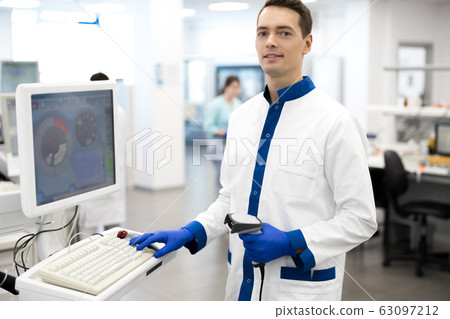 Smiling male scientist using lab machine for pathology blood test Smiling male scientist using lab machine for pathology blood test 63097212