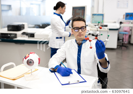 Research scientist in lab coat looking at molecule model 63097641