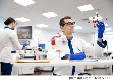 Male research scientist looking at amino acid molecule model Male research scientist looking at amino acid molecule model 63097642