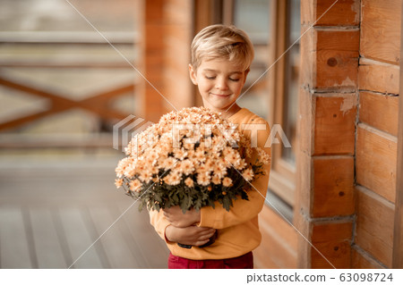 A 7-year-old boy holds a bouquet of flowers near a village wooden house 63098724