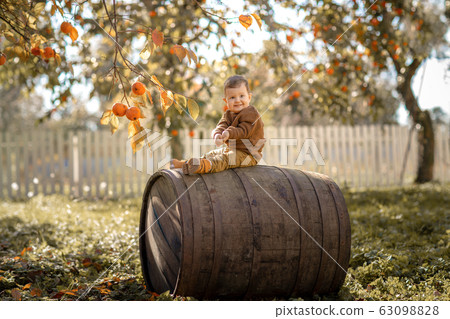 A 3-year-old boy sits on a large wooden barrel 63098828