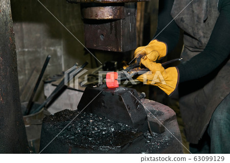 female hands processes a red hot workpiece with a 63099129