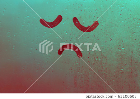 Foggy glass on window raindrops with drawn sad face eyes closed in green red gradient concept photo Foggy glass on window raindrops with drawn sad face eyes closed in green red gradient concept photo 63100605