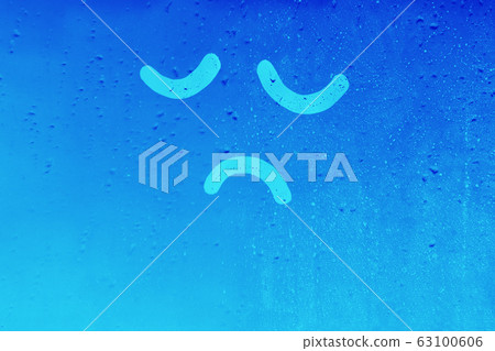 Foggy glass on window raindrops with drawn sad face eyes closed in blue color concept photo Foggy glass on window raindrops with drawn sad face eyes closed in blue color concept photo 63100606