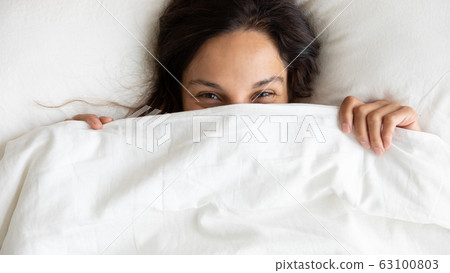 Smiling young woman hide under blanket waking up 63100803