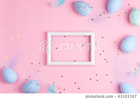 Corner frame from handmade painted eggs of pastel blue colors, photo frame and light feathers on a light pink background. 63101387