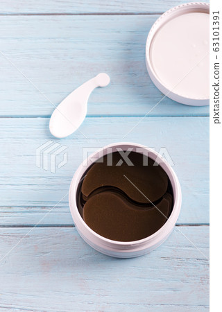 Cosmetics collagen brown patches in a plastic jar for skin around the eyes on a light blue wooden background. 63101391
