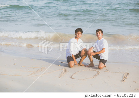 Young asian couple gay smiling romantic drawing word text love together on sand in vacation 63105228